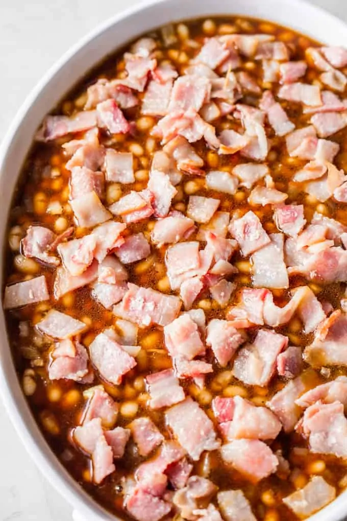 Beans in a baking dish topped with partially cooked bacon to make baked beans.