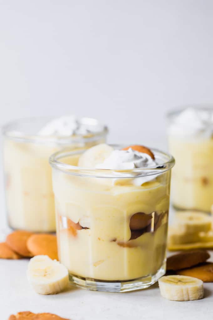 Jars filled with layers of vanilla pudding, Nilla wafers, and sliced bananas. Topped with whipped Cream. Surrounded by Nilla wafers and banana slices.