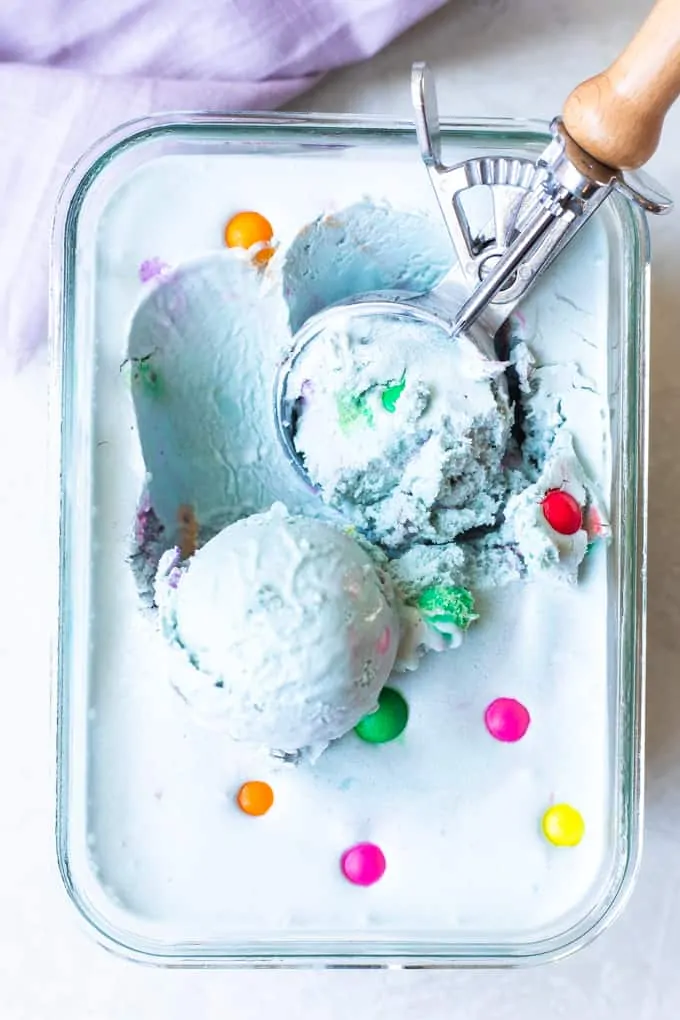 Glass container filled with bubble gum ice cream being scooped up with an ice cream scoop that has a wooden handle.