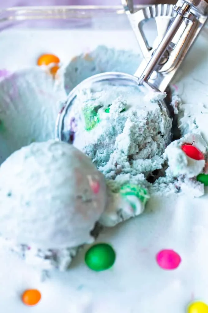 An ice cream scoop scooping up light blue colored bubble gum ice cream.