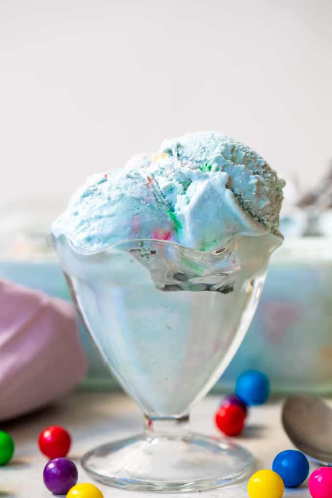 Glass ice cream cup filled with light blue colored bubble gum ice cream that has colorful gumballs inside.
