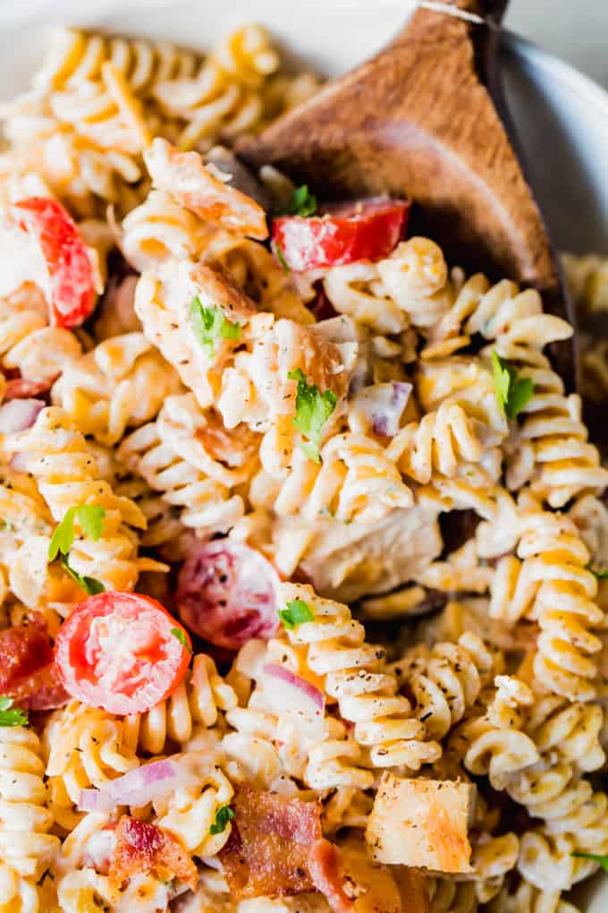 A wooden spoon in a white bowl filled with chicken bacon ranch pasta salad.