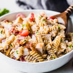 White bowl filled with homemade chicken pasta salad with a wooden serving spoon.