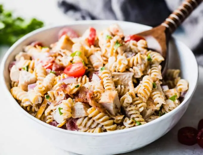 White bowl filled with homemade chicken pasta salad with a wooden serving spoon.