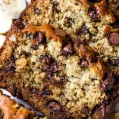 Sliced loaf of chunky monkey banana bread showing banana bread with chunks of walnut, and melted chocolate chips. Slices of bananas and walnuts on the side.