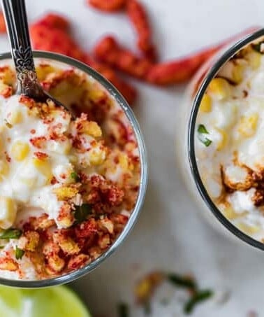 Cups filled with mexican street corn topped with hot cheetos and chili sauce.
