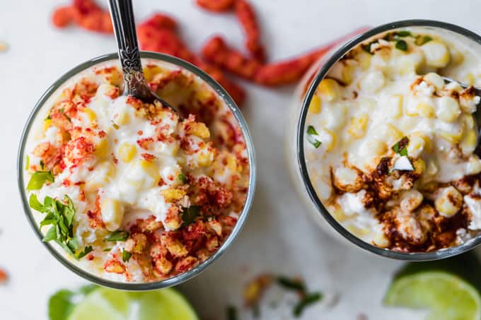 Cups filled with mexican street corn topped with hot cheetos and chili sauce.