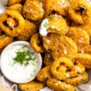 Basket of fried pickles with fried jalapeños and a bowl of ranch topped with fresh herbs.