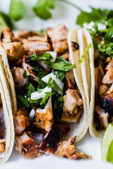 Grilled chicken street tacos laid next to each other with wedges of lime off to the side.