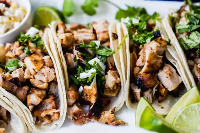 Grilled chicken street tacos laid next to each other with wedges of lime off to the side. 
