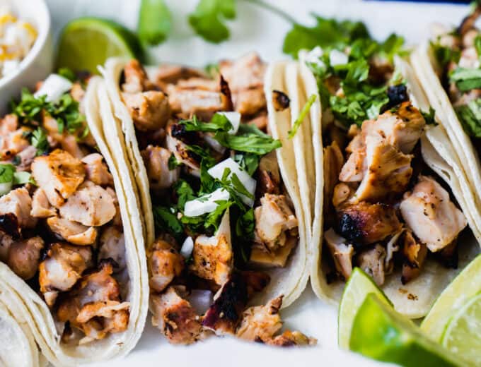 Grilled chicken street tacos laid next to each other with wedges of lime off to the side.