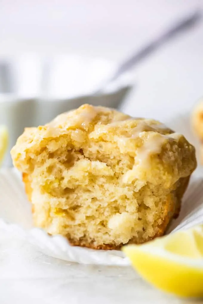 Lemon muffin in a white paper, with a bite missing showing the texture of the baked muffin.