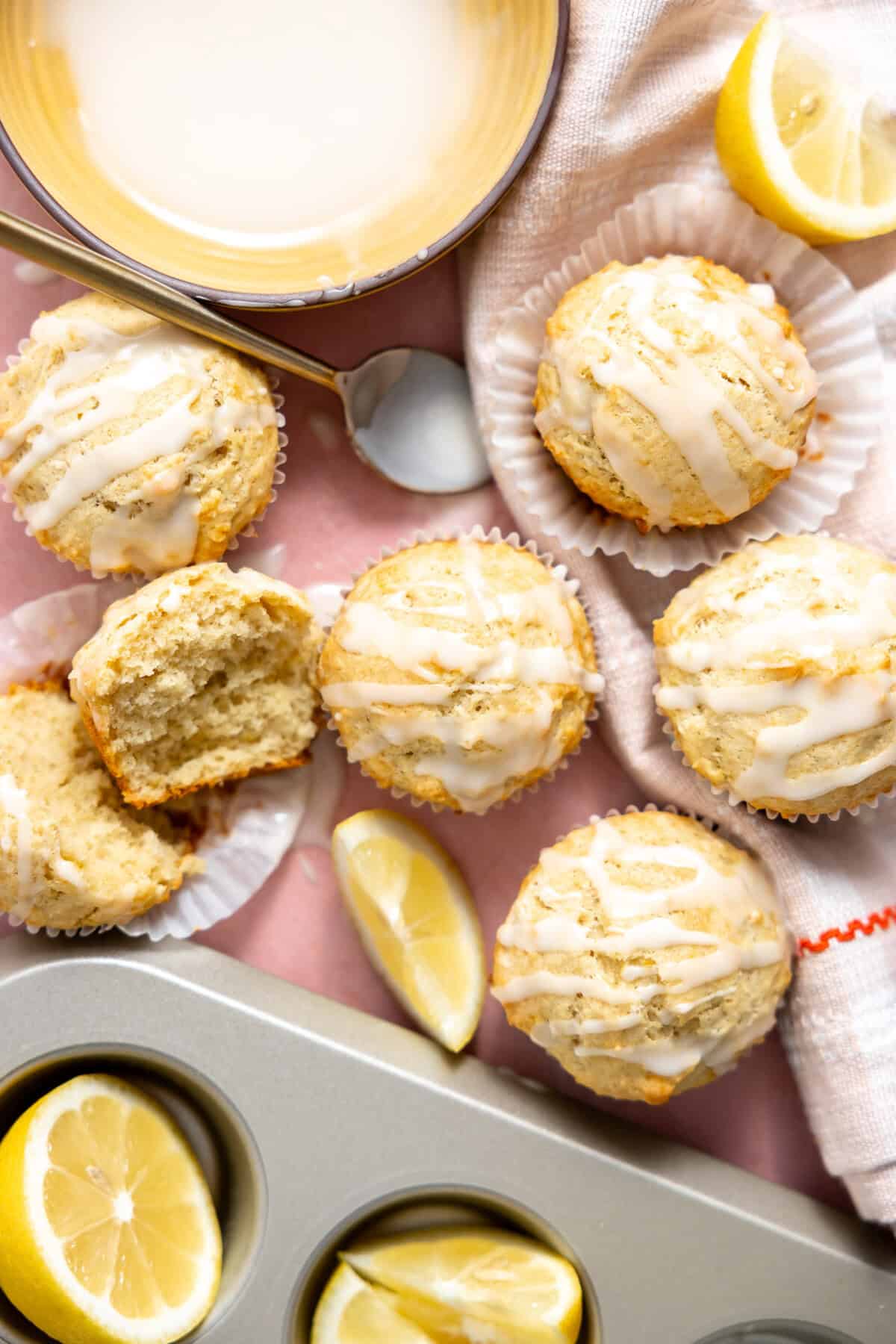 Lemon muffins laid out on the counter with a bowl of glaze on the side. 