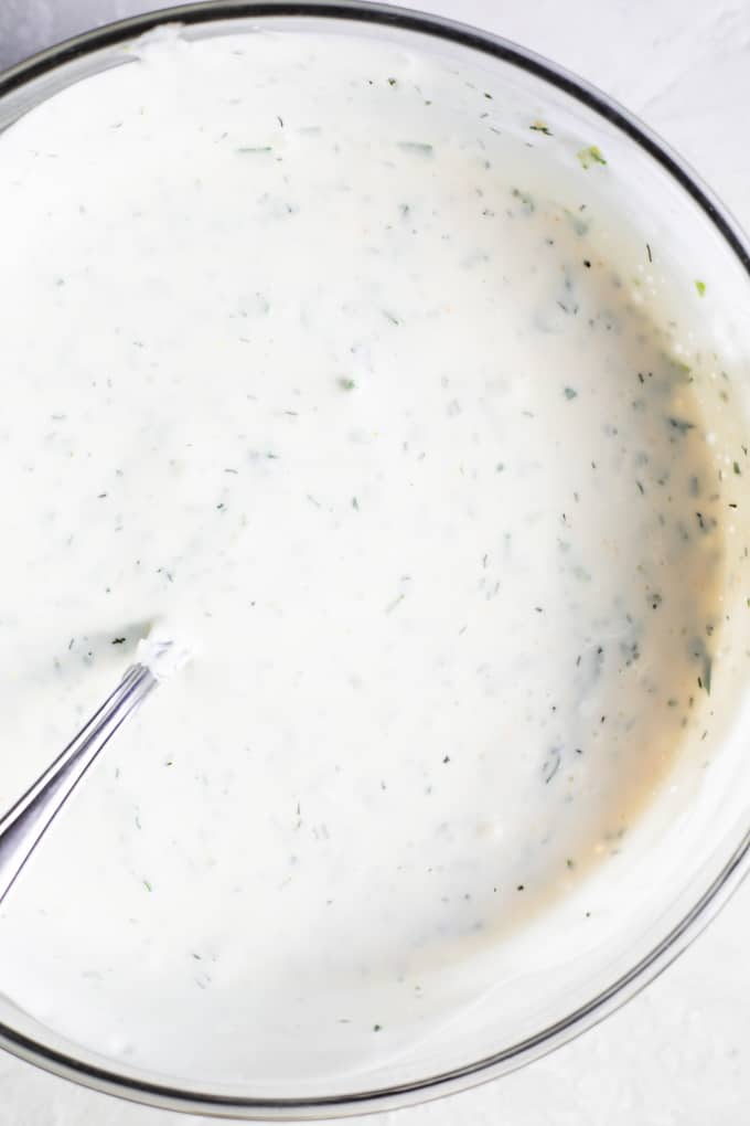 Glass bowl filled with homemade creamy ranch dressing just stirred around to mix. 