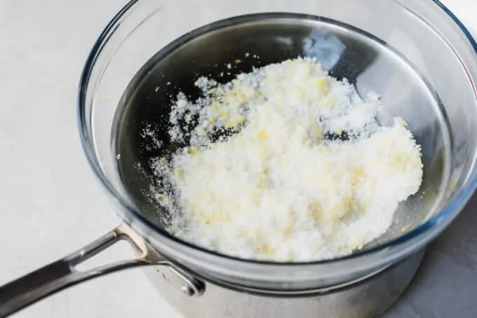 Double boiler made with a saucepan and a glass bowl filled with sugar and lemon zest.