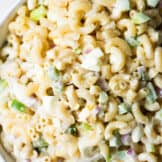Large white bowl filled with macaroni salad, elbow macaroni noodles, green bell pepper, hard boiled egg, and red onion all tossed in a creamy dressing.