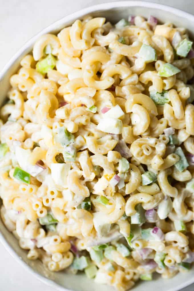Large white bowl filled with macaroni salad, elbow macaroni noodles, green bell pepper, hard boiled egg, and red onion all tossed in a creamy dressing.