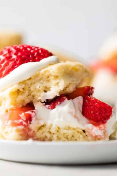 Strawberry shortcake made with a sweet shortcake biscuit, layers of biscuit, whipped cream and strawberries served on a white plate.