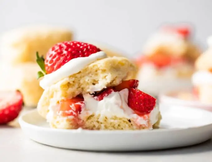 Strawberry shortcake made with a sweet shortcake biscuit, layers of biscuit, whipped cream and strawberries served on a white plate.