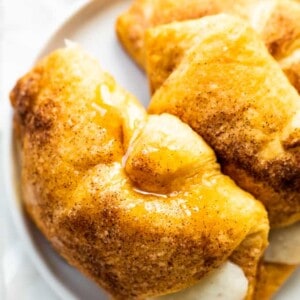 Overhead view of three sopapilla cheesecake rolls on a white plate, cinnamon sticks on the side.