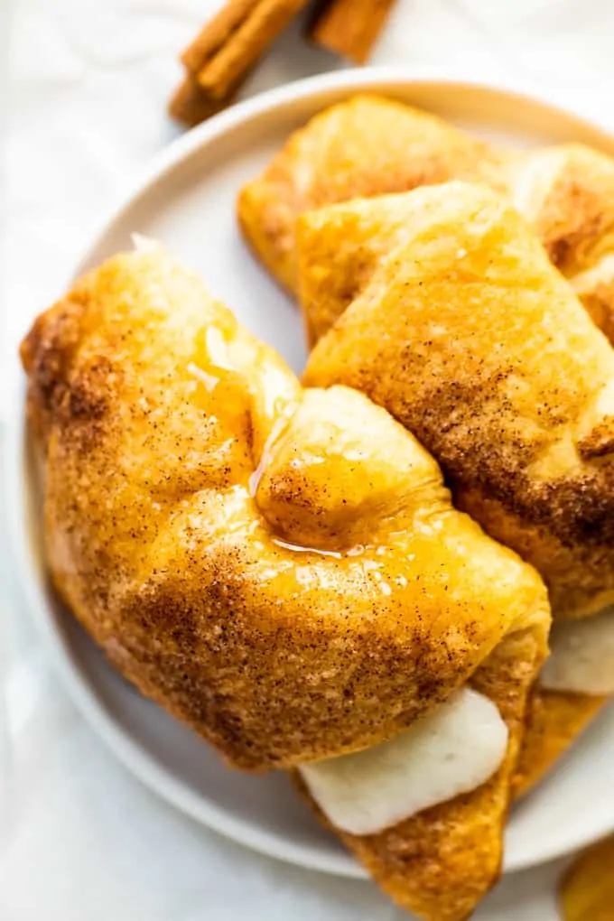 Overhead view of three sopapilla cheesecake rolls on a white plate, cinnamon sticks on the side.