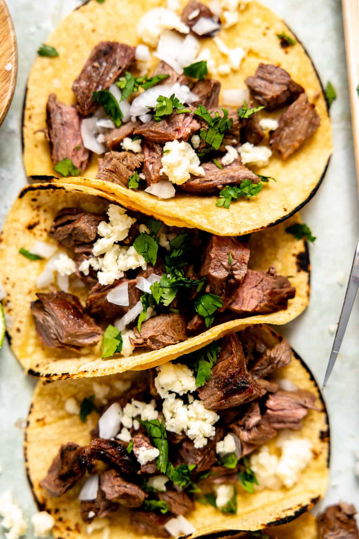 Chopped carne asada on corn tortillas topped with cilantro, onion, and crumbled queso fresco. 