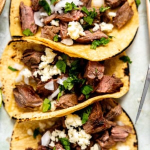 Chopped carne asada on corn tortillas topped with cilantro, onion, and crumbled queso fresco.