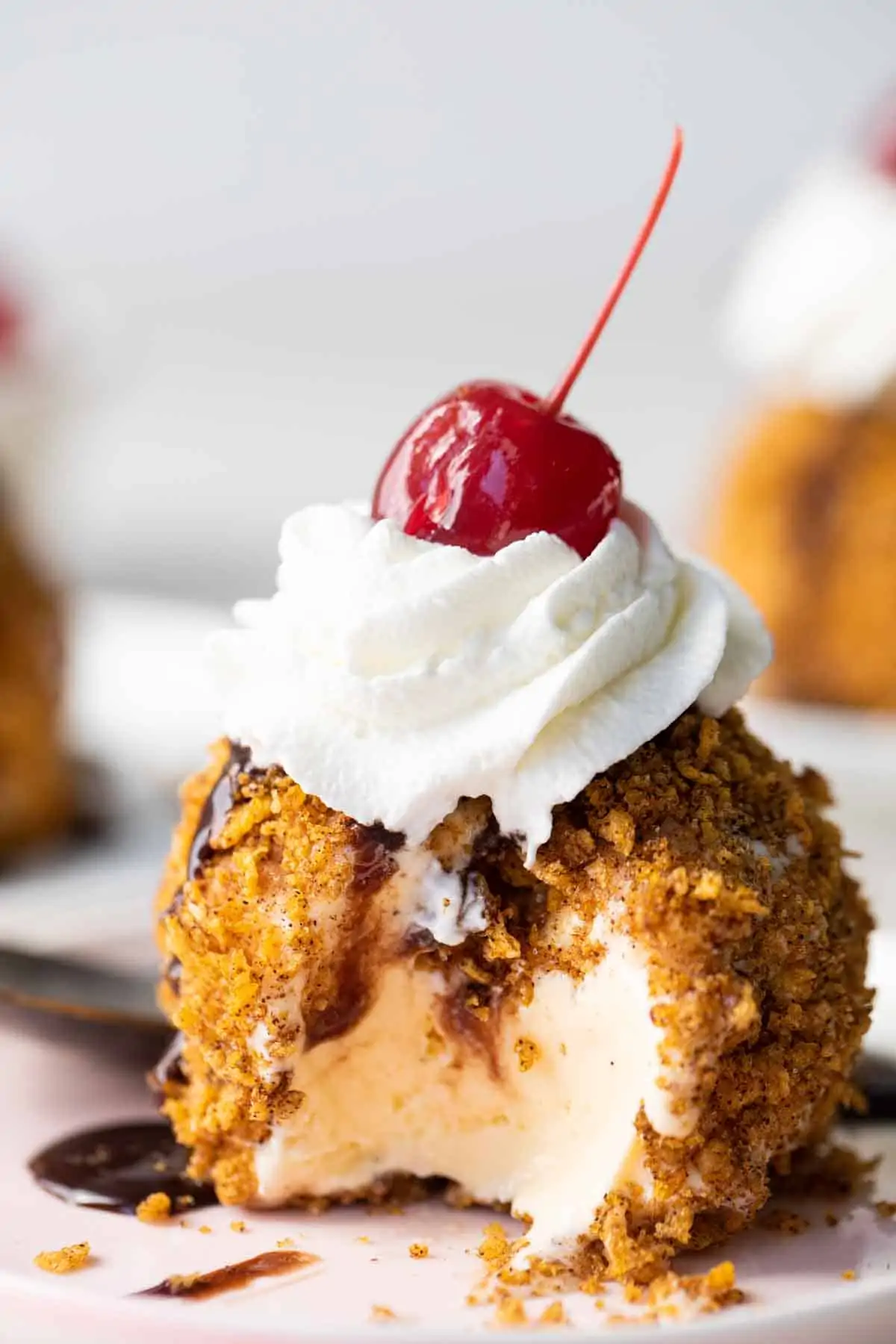 Mexican Fried Ice Cream topped with whipped cream and a cherry with a bite taken out on a plate.
