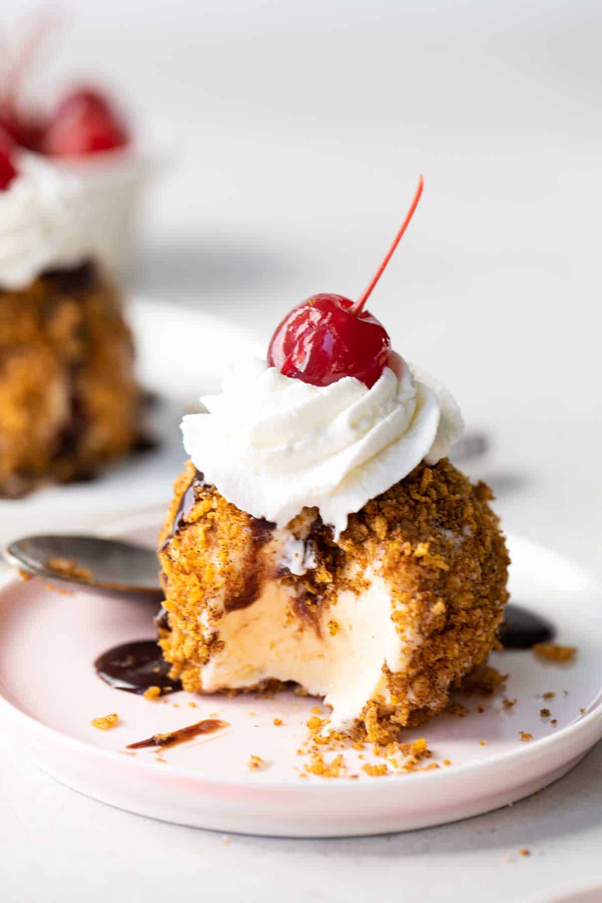 Mexican Fried Ice Cream topped with whipped cream and a cherry with a bite taken out on a plate.