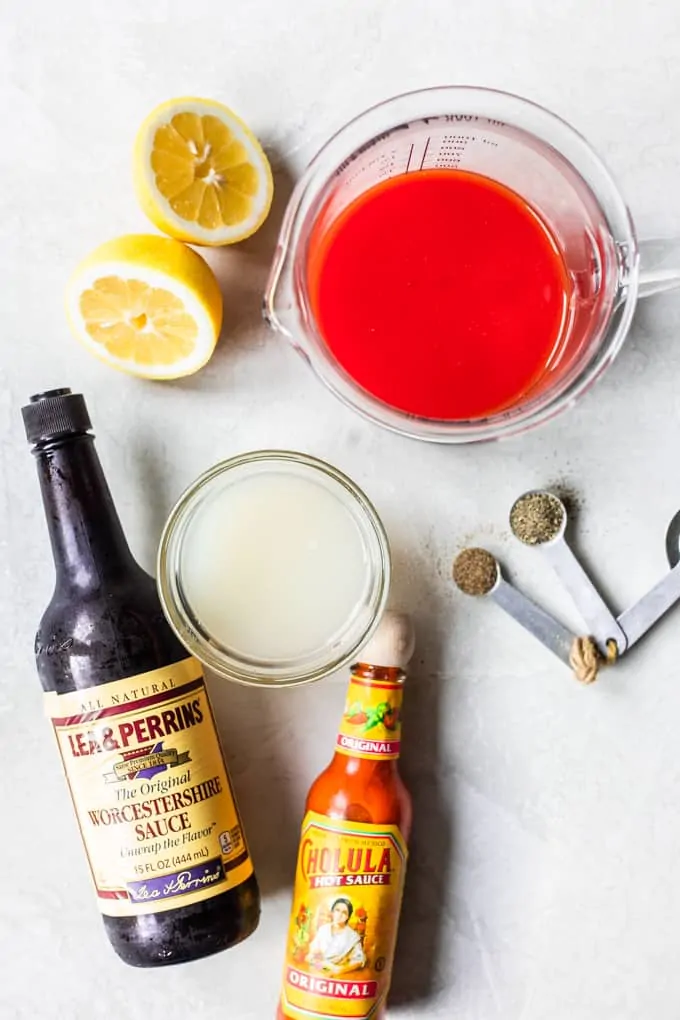 Ingredients needed to make homemade Clamato juice, showing a measuring cup of tomato juice, lemon juice, clam juice, celery salt, Worcestershire sauce, and hot sauce.