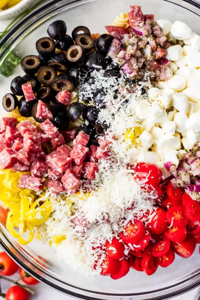 Overhead view of ingredients for Italian pasta salad in a glass bowl.