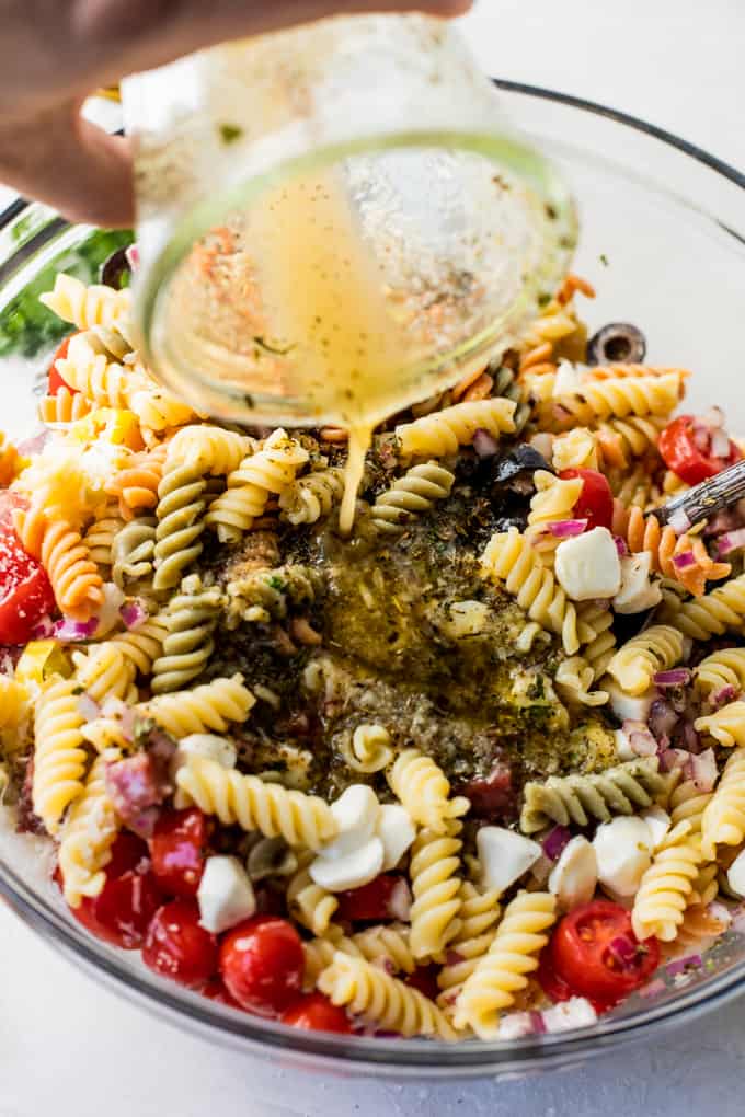 Italian dressing being poured over the top of pasta salad.