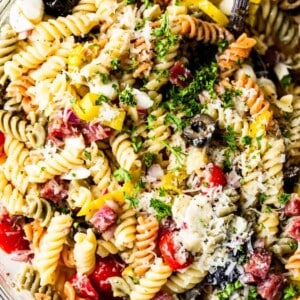 Close up view of rotini noodles with tomatoes, olives, salami, mozzarella, pepperoncinis, and shredded parmesan and fresh parsley, coated in Italian dressing.