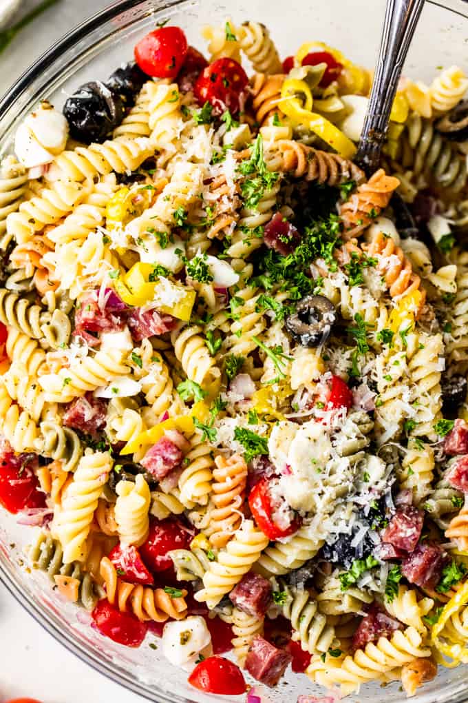 Close up view of rotini noodles with tomatoes, olives, salami, mozzarella, pepperoncinis, and shredded parmesan and fresh parsley, coated in Italian dressing. 