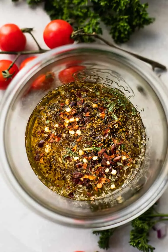 Overhead view of jar filled with oil, vinegar, honey, and spices and herbs to make Italian dressing.