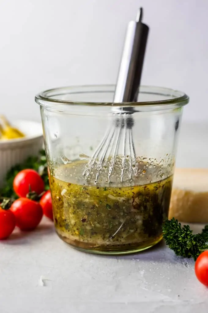 Jar filled with ingredients for homemade Italian dressing with a whisk to mix together.