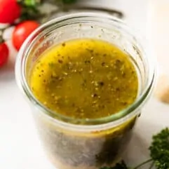 Jar filled with homemade Italian dressing, with tomatoes on the side and fresh parsley.