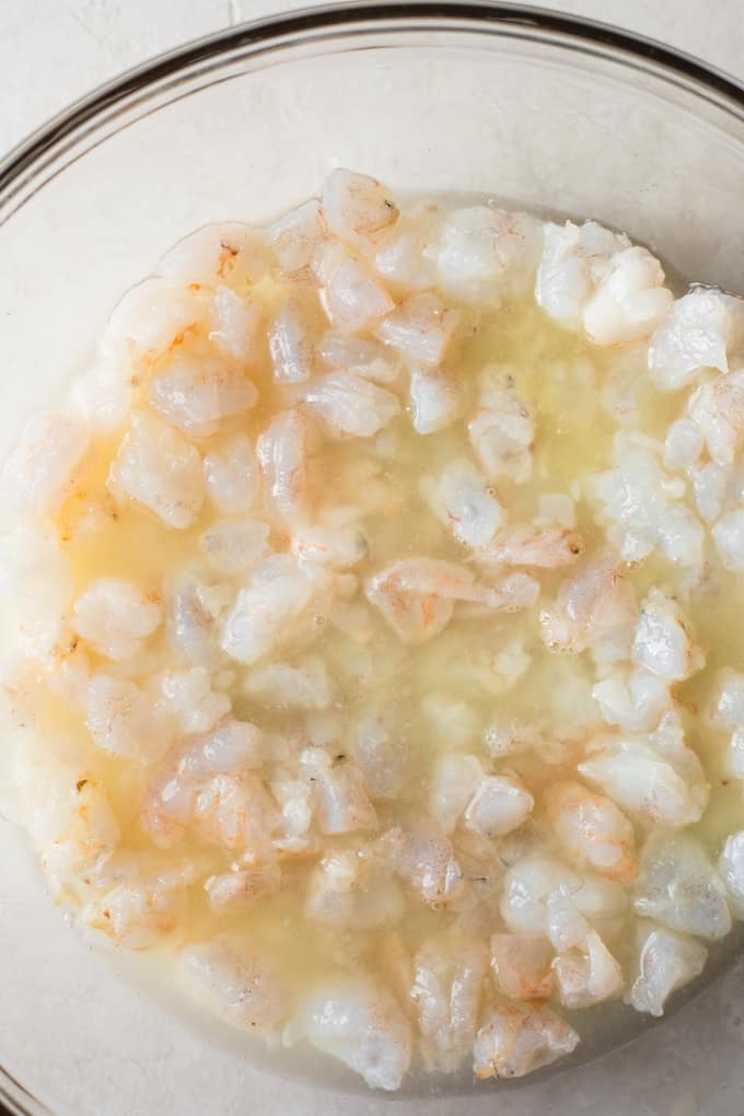 Chopped shrimp covered in lemon juice in a medium size glass bowl.