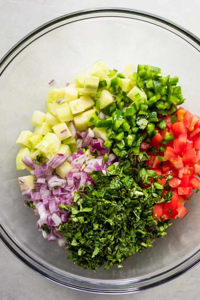 Glass bowl filled with diced cucumber, red onion, jalapeño, tomato, and cilantro.