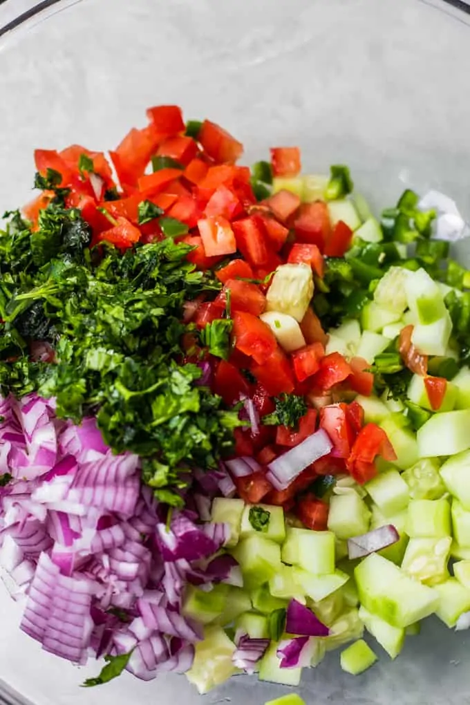 Glass bowl filled with diced red onion, cucumber, jalapeno, tomato and cilantro 