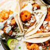 Tray filled with shrimp tacos that are topped with crumbled queso fresco, and drizzled with a cilantro lime Crema.