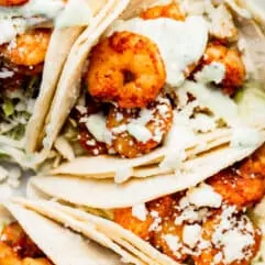 Corn tortillas layered and filled with shredded cabbage, cooked shrimp coated in a red seasoning blend, topped with crumbled queso fresco, and drizzled with a cilantro lime Crema.