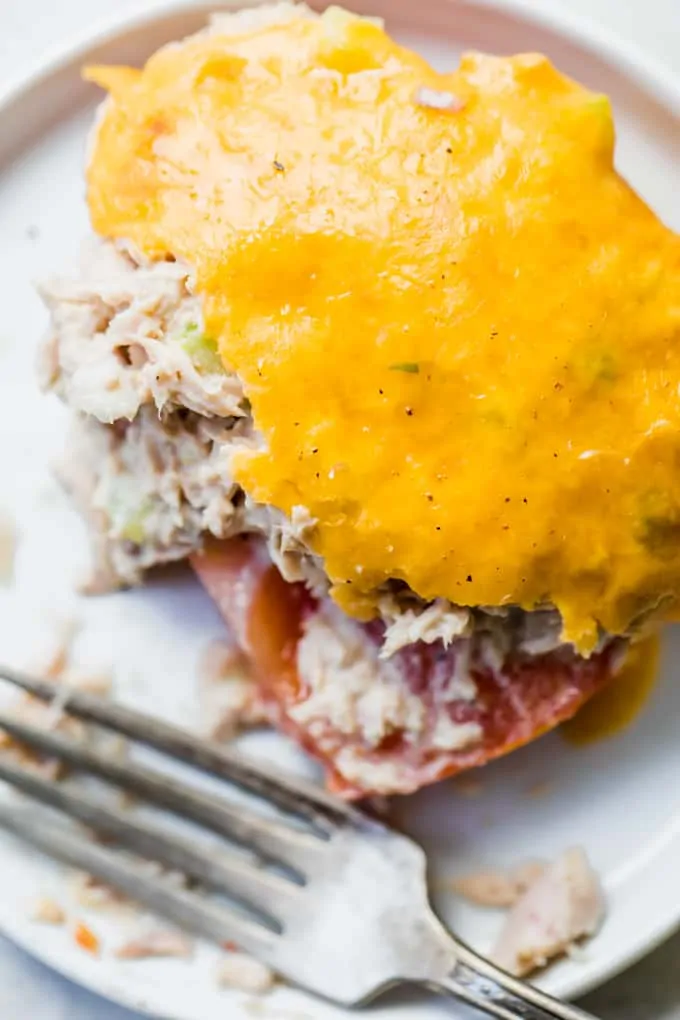 Overhead shot of melted cheese over tuna salad on top of thick sliced tuna, with a fork laying on the side on a white plate.