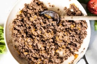 Skillet filled with cooked ground beef that has melted cheddar cheese.