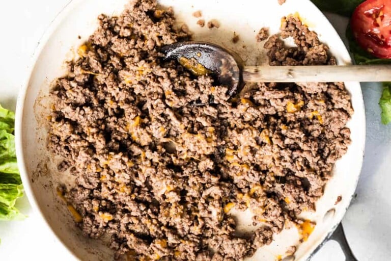 Skillet filled with cooked ground beef that has melted cheddar cheese.