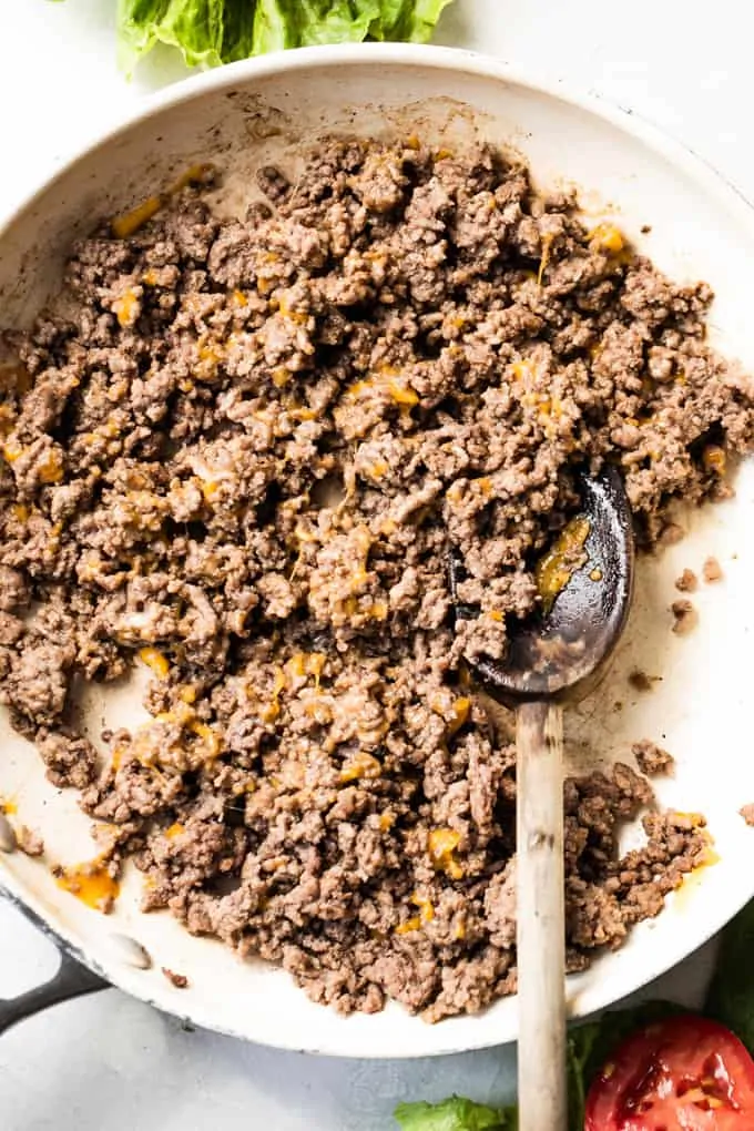 Skillet filled with cooked ground beef that has melted cheddar cheese.