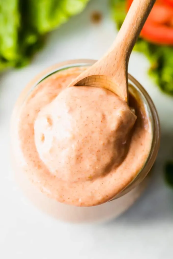 Overhead view of a wooden spoon scooping up burger sauce from a small glass jar.