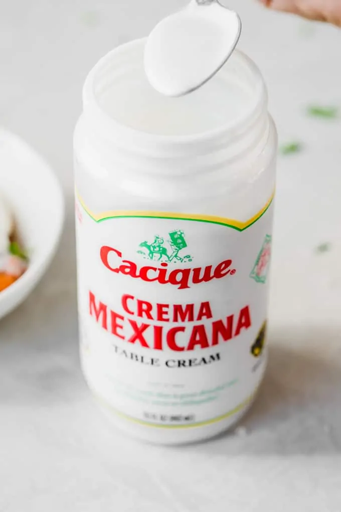 Spoon dipping into a jar of Cacique Crema Mexicana.