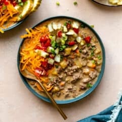 Bowl filled with cheeseburger soup and topped with diced tomatoes, pickles, cheese and herbs.