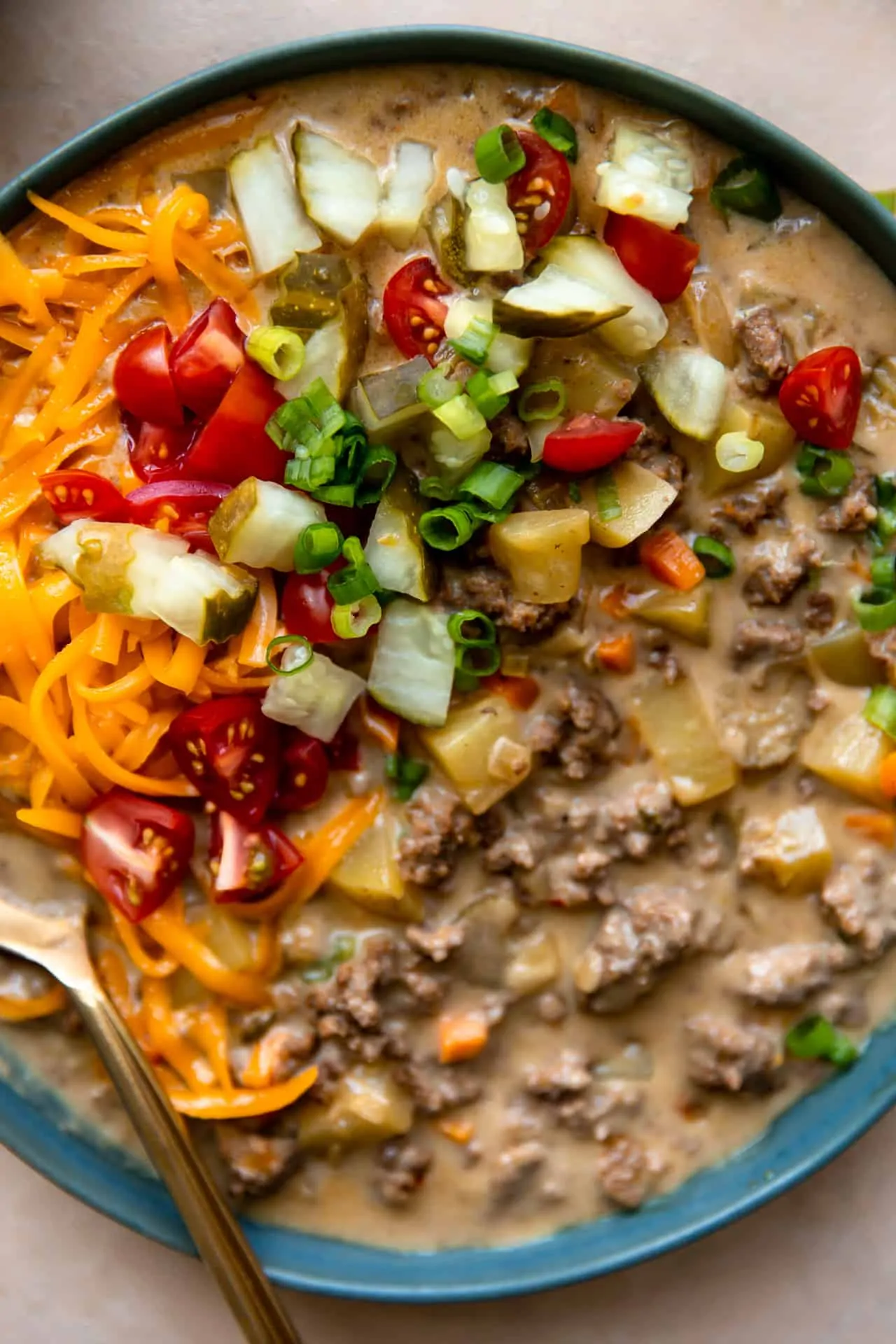 Up close view of the cheeseburger soup in a bowl topped with shredded cheese, diced pickle, green onion and tomato. 